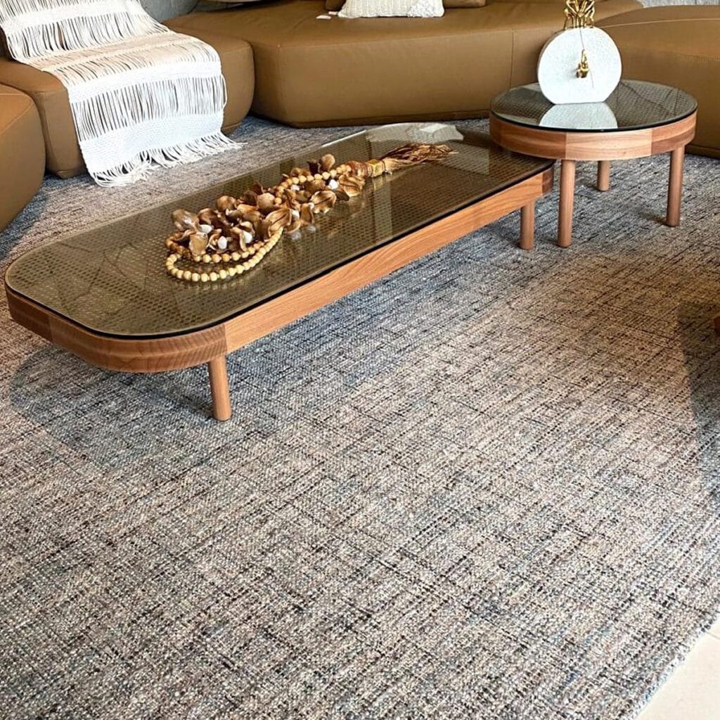 Tapete texturizado sob medida instalado em sala de estar com sofá caramelo e mesas de centro em madeira, solução da Copato.